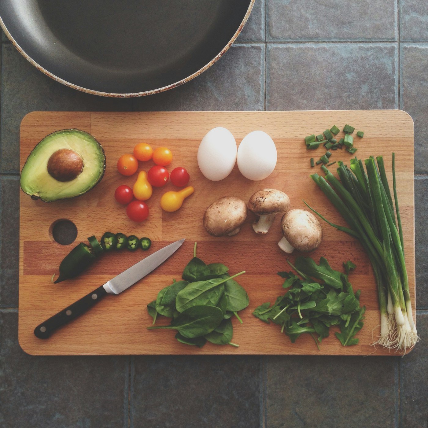 Fresh vegetables, eggs, mushrooms, and herbs arranged on a wooden cutting board